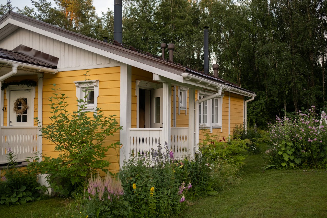 services-04 A picturesque yellow cottage surrounded by lush greenery and summer blooms in a peaceful rural area.