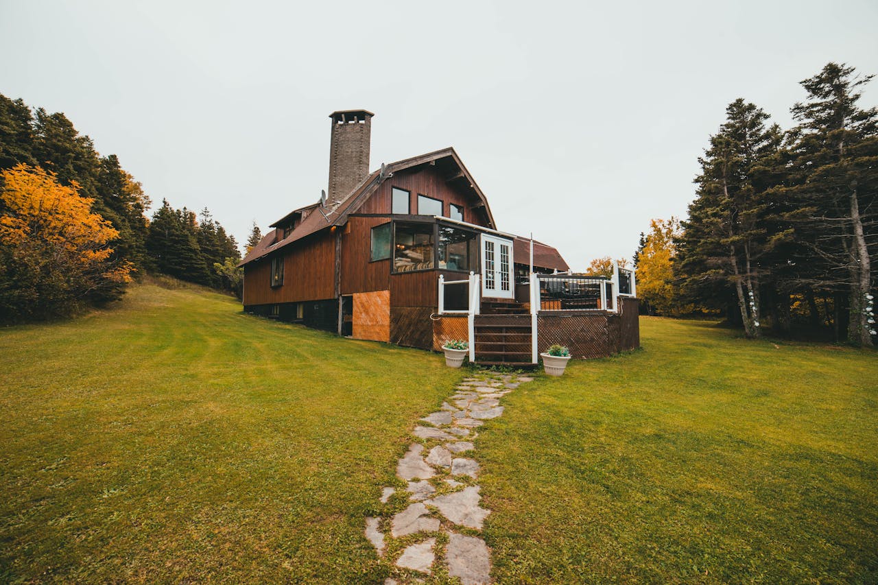 Rustic wooden cabin surrounded by autumn trees and lush greenery, featuring a stone path leading up to the entrance.